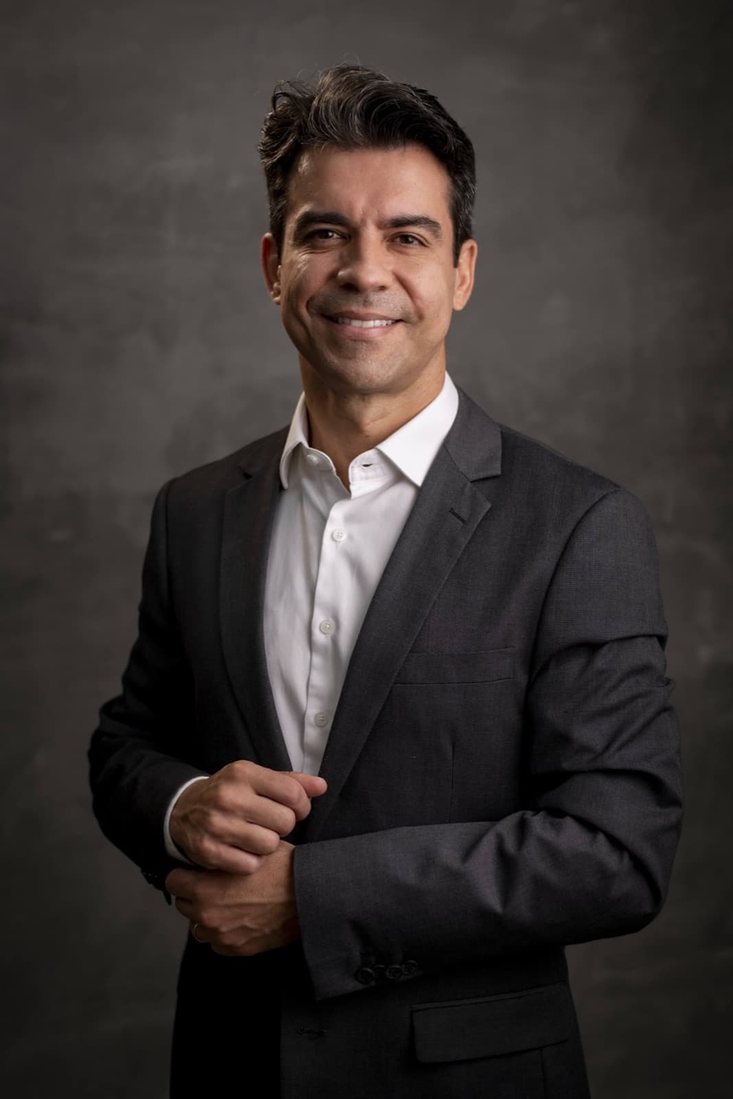 Dr. Fernando Thomazinho sorrindo, de terno cinza, em retrato de estúdio
